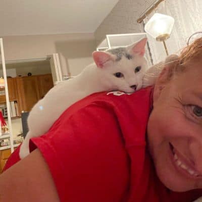 White cat cuddling on pet sitter’s back – loving in-home cat sitting service.
